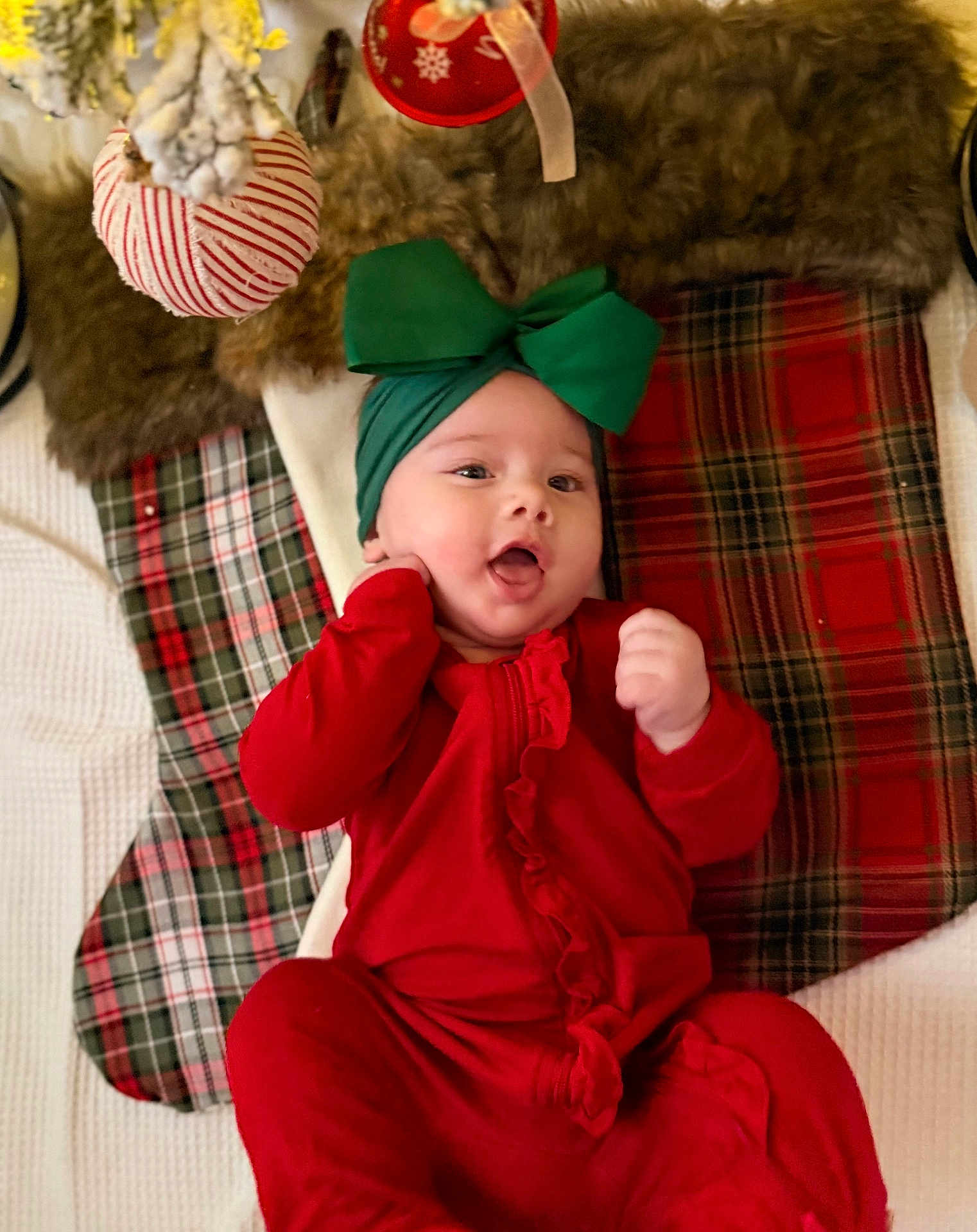 Haisley joined the competition — help win amazing prizes! baby, infant, red_clothing, green_bow, headband, plaid_stockings, holiday_decorations, christmas, festive, cute, smiling, indoors, cozy, soft_texture, blanket, child, portrait, happy, celebration, seasonal
