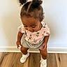 toddler, child, hair_buns, curly_hair, floral_top, gray_shorts, white_shoes, wooden_floor, indoor, playful, cute, smiling, person, standing, young_child, fashion, casual_clothing, happy, baby, portrait