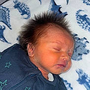 Freddie is registered to the contest to win money with this photo: newborn, baby, sleeping, hair, onesie, star_pattern, blanket, dinosaur_print, face, peaceful, infant, cute, portrait, child, soft, cozy, resting, indoors, closeup, young