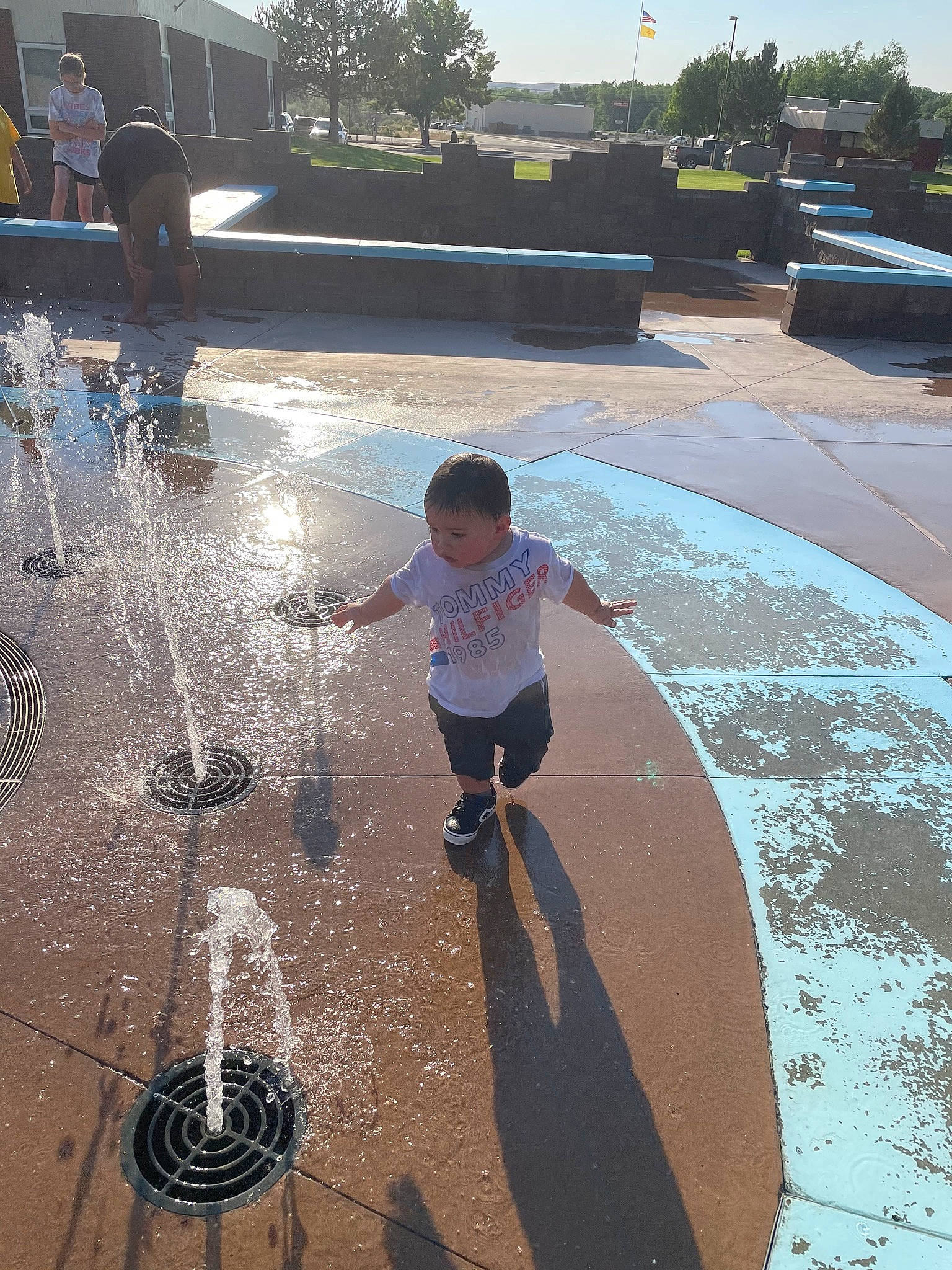 Thadd is registered to the contest to win money with this photo: asphalt, child, city, concrete, flooring, font, fountain, fun, grass, leisure, light, person, play, recreation, road_surface, sidewalk, sky, toddler, tree, water