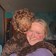 Piper Lou is registered to the contest to win money with this photo: person, dog, indoor, hugging, smiling, curly_fur, brown_dog, casual_clothing, cozy, face, portrait, happy, animal, pet, companion, friendship, furniture, blue_wall, mirror, home