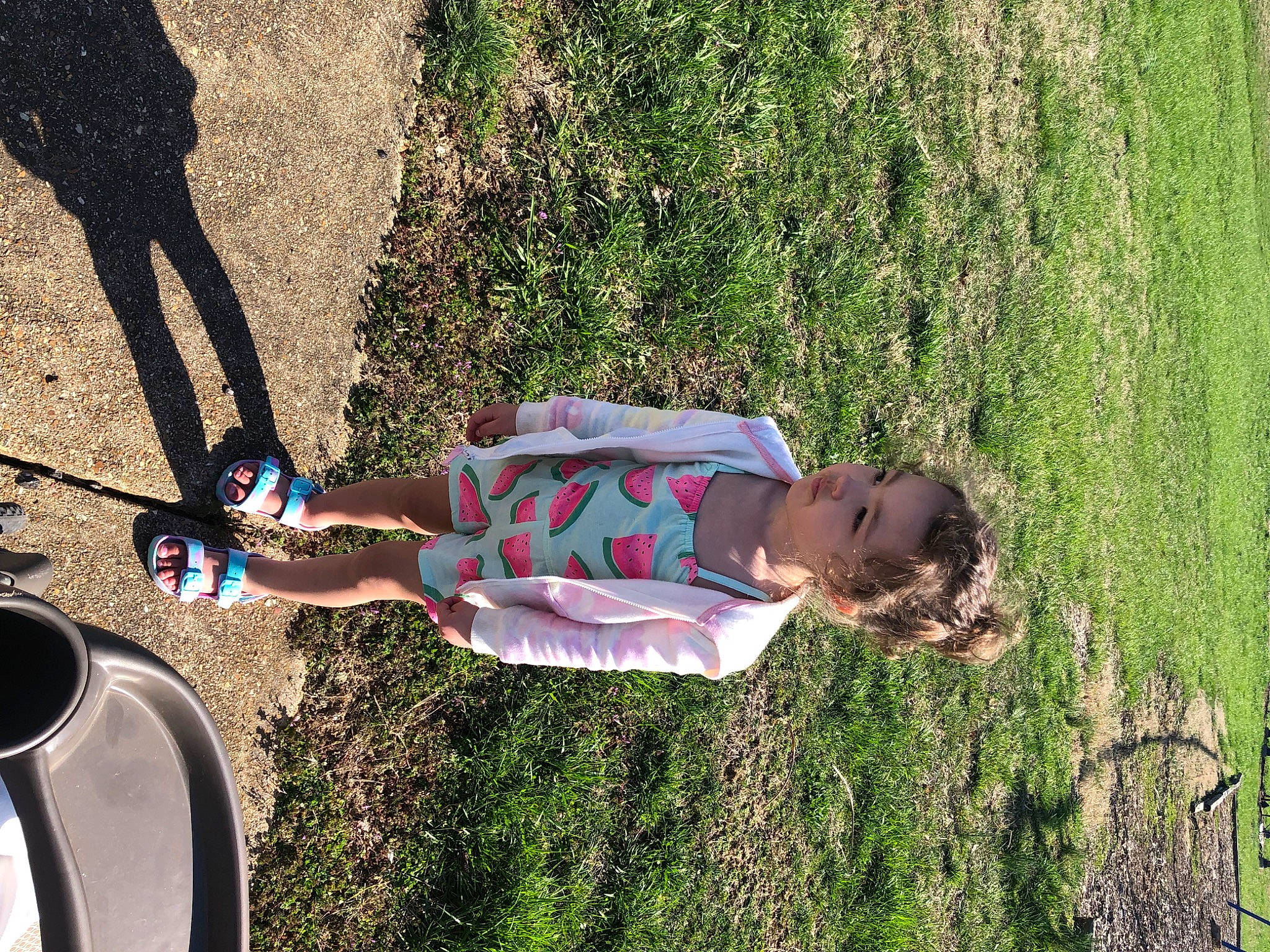 Kya is registered to the contest to win money with this photo: asphalt, automotive_tire, fun, grass, grass_family, happy, human_leg, landscape, leisure, people_in_nature, person, plant, recreation, shadow, shrub, soil, summer, tints_and_shades, tire, toddler