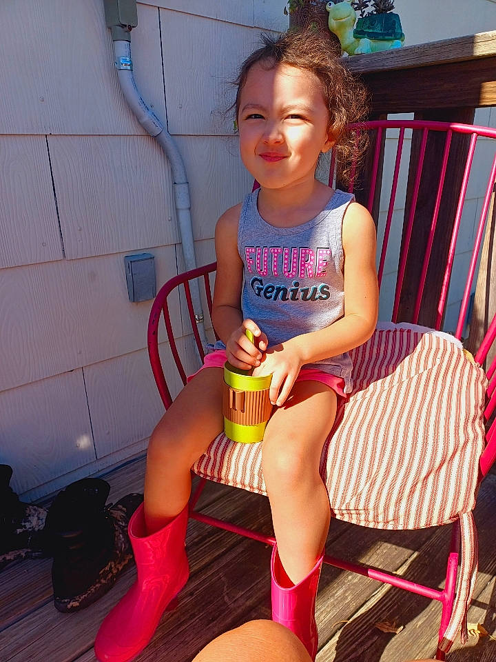 Kya is registered to the contest to win money with this photo: chair, dress, facial_expression, foot, fun, hair, happy, human_leg, joy, knee, lap, leg, leisure, magenta, person, pink, sandal, shorts, shoulder, sitting