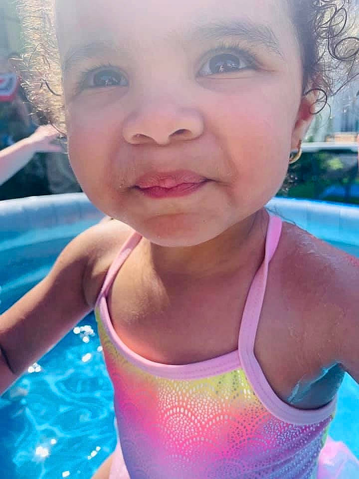 Malia is registered to the contest to win money with this photo: cheek, chest, child, face, facial_expression, fun, happy, leisure, lip, mouth, neck, nose, person, skin, smile, summer, swimming_pool, toddler, tooth, vacation