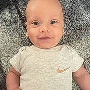 Isaiah is registered to the contest to win money with this photo: baby, infant, smiling, face, eyes, clothing, nike, onesie, carpet, texture, skin, person, cute, happy, lying_down, child, toddler, indoors, portrait, casual