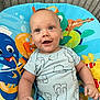 baby, child, onesie, blue, smile, play_mat, sea_creatures, cartoon, happy, infant, cute, face, clothing, sitting, indoor, bright, young, cute_expression, person, baby_toy