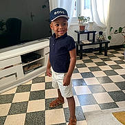 Naïs a rejoint le concours — aidez-le/la à gagner de superbes lots ! child, boy, smile, cap, indoor, floor, checkered_floor, shorts, sandals, polo_shirt, window, plant, table, television, cabinet, curtains, home, furniture, happy, standing