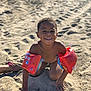 child, smiling, beach, sand, floaties, water_wings, sunlight, happy, playing, outdoor, bare_chest, summer, fun, toddler, vacation, skin, toy, recreation, sunny, daytime