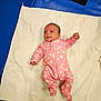 baby, infant, pink_onesie, flower_pattern, blanket, white_blanket, blue_surface, smartphone, lying_down, newborn, cute, child, portrait, indoor, clothing, person, baby_girl, soft_texture, quilted, relaxing