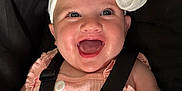 Elsie-Mae is registered to the contest to win money with this photo: baby, child, smile, happy, headband, bow, pink_clothing, straps, harness, face, closeup, infant, cute, portrait, cheerful, young_child, human, sitting, apparel, expression