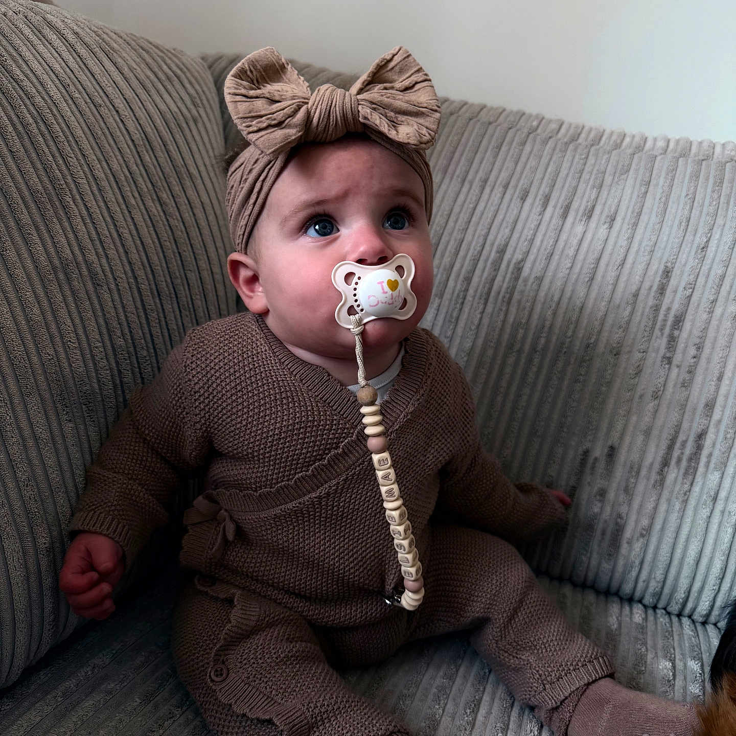 Elsie-Mae joined the competition — help win amazing prizes! baby, beaded_clip, bow, buttoned_pants, child, couch, cozy, curious, cute, headband, indoors, infant, knitted_clothing, pacifier, portrait, sitting, sock, soft_lighting, textured_couch, young_child