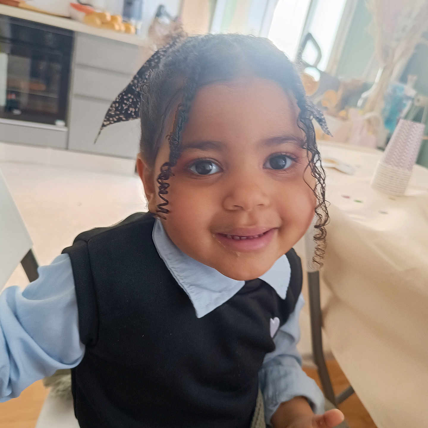 Ina-Maria a rejoint le concours — aidez-le/la à gagner de superbes lots ! chair, child, clothing, cozy, curly_hair, face, furniture, happy, home, indoor, kitchen, natural_light, person, portrait, ribbon, shirt, smiling, sweater, table, window