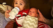 Joseph is registered to the contest to win money with this photo: toddler, baby, bottle, swaddle, pajamas, family, adult, beard, couch, blanket, indoor, child, holding, comfort, bedroom, striped_clothing, red_clothing, white_clothing, relaxed, parent