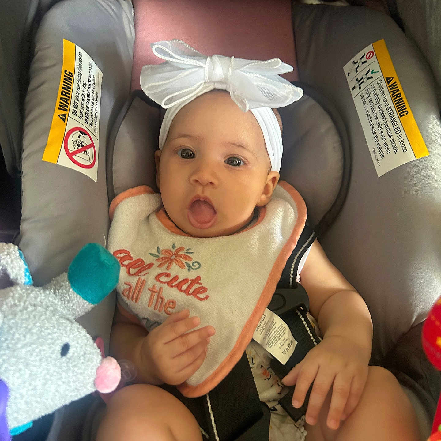 Noveli joined the competition — help win amazing prizes! baby, bib, bow, car_seat, child, closeup, clothing, cute, expression, face, happy, headband, indoor, infant, person, safety_harness, seat_belt, soft_toy, tongue_out, toy