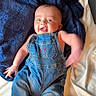 arms, baby, bed, blue_blanket, child, clothing, cute, denim_overalls, fabric, face, happy, head, indoors, infant, joyful, legs, person, portrait, smiling, textile
