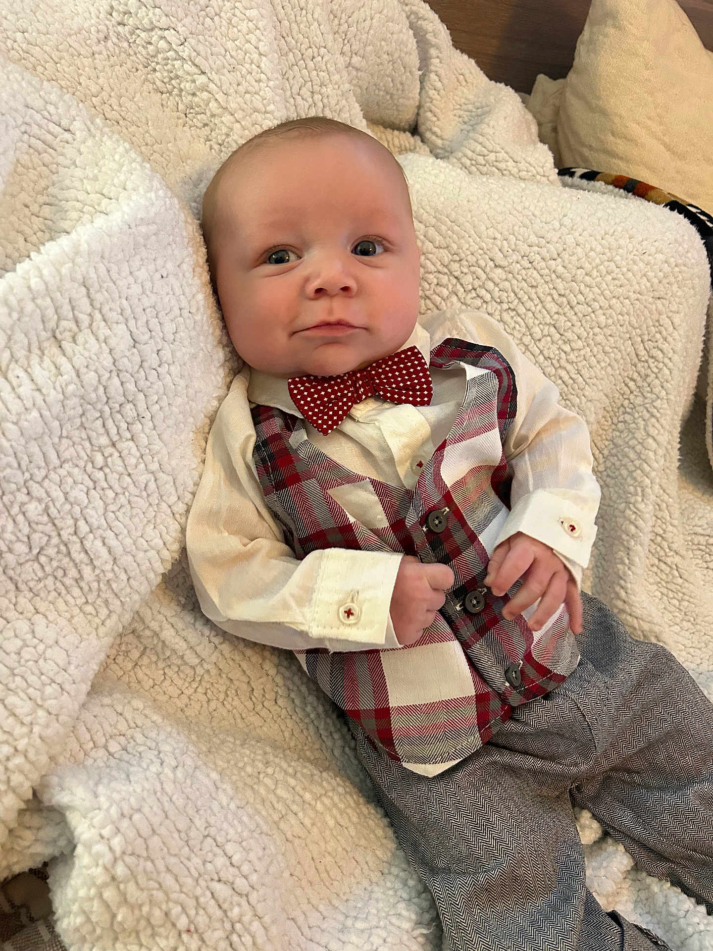 Jase is registered to the contest to win money with this photo: baby, infant, bow_tie, plaid_vest, blanket, cozy, pillow, shirt, pants, hands, face, eyes, cheeks, portrait, smile, button, fabric, couch, home_interior, gentleman