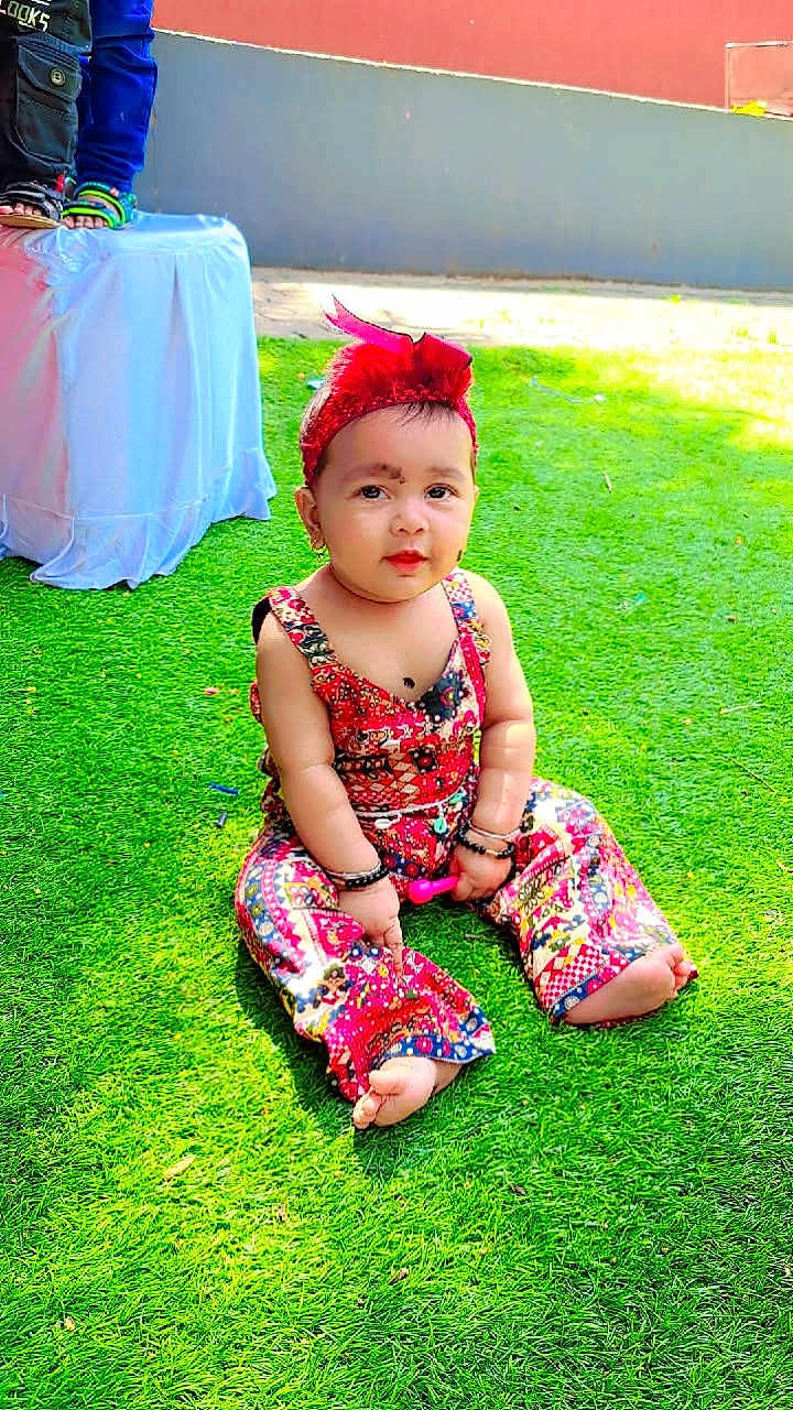 Mirha joined the competition — help win amazing prizes! baby, child, grass, outdoor, colorful_clothing, headband, sitting, curious, playful, patterned_outfit, barefoot, bracelets, sunlight, greenery, young_child, portrait, cute, casual, daylight, relaxed