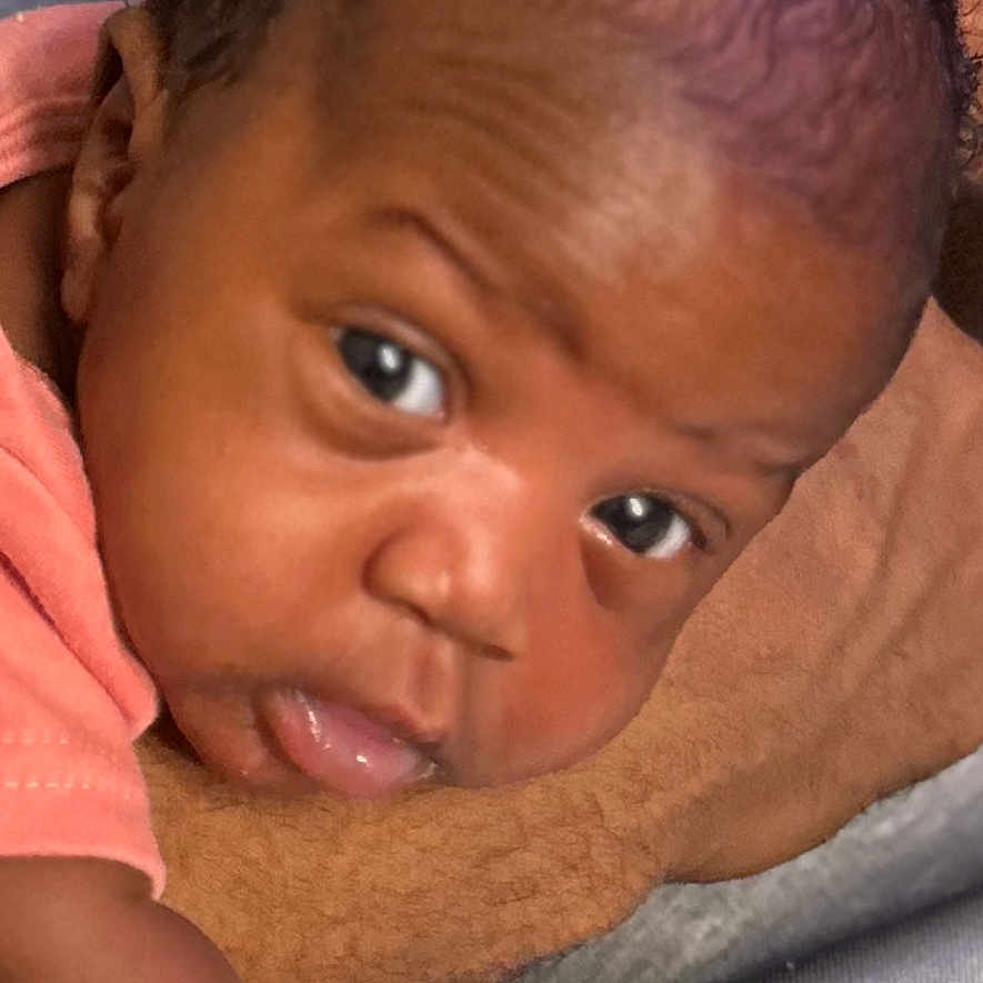 Azalea is registered to the contest to win money with this photo: baby, child, close_up, curly_hair, cute, expression, eyes, face, head, indoors, infant, lying_down, newborn, peach_clothing, person, portrait, resting, skin, soft_surface, young