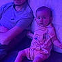 baby, barefoot, cap, casual_clothing, child, couch, expression, face, furniture, home, indoor, infant, legs, man, people, portrait, purple_light, relaxing, sitting, tshirt