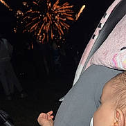 Lyla participe au concours pour gagner de l'argent avec cette photo : baby, blanket, celebration, clothing, colorful, dark, ear, event, face, fireworks, hand, infant, light, night, outdoor, pacifier, people, sky, stroller, toy