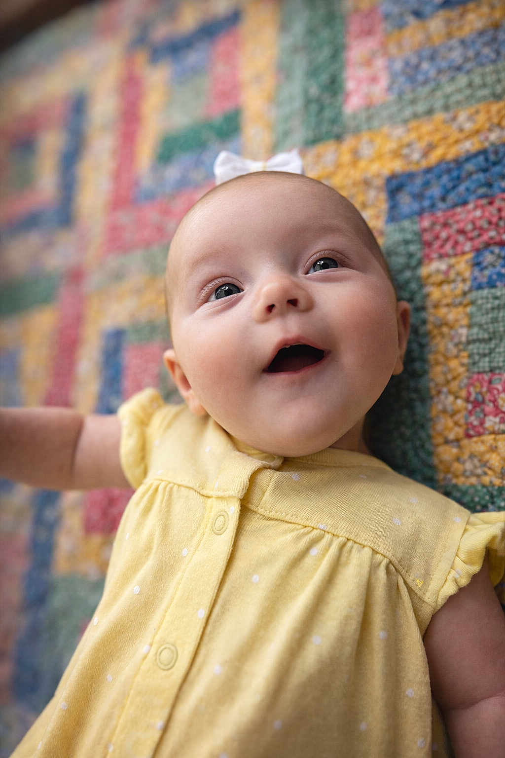 Harper is registered to the contest to win money with this photo: baby, infant, yellow_dress, polka_dots, quilt, colorful, smiling, happy, face, child, lying_down, cute, closeup, portrait, indoors, soft_light, headband, expression, skin, eyes