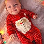 Harper joined the competition — help win amazing prizes! baby, child, infant, red_onesie, santa_claus_design, christmas_lights, holiday, smiling, lying_down, blanket, soft_texture, festive, cute, indoors, portrait, happy, face, hands, feet, cozy