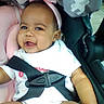 baby, child, car_seat, pink_headband, smile, happy, infant, safety_harness, cute, indoor, seated, clothing, closeup, person, headwear, soft_toy, baby_girl, cheerful, portrait, seat_belt