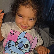 Isamary Sepulveda is registered to the contest to win money with this photo: blue_character, cartoon, child, couch, curly_hair, curtain, dark_hair, eyes, face, grinning, home, indoor, photography, pink_clothing, portrait, sitting, smiling, stitch, t_shirt, toddler