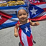 baby, child, clothing, dress, flag, happy, headband, market, merchandise, outdoor, patriotic, portrait, puerto_rican_flag, red_white_blue, sandals, smiling, sunlight, toddler, vendor_stall, walking