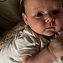 baby, infant, child, person, face, skin, arm, tattoo, onesie, clothing, lying_down, indoor, closeup, curious, expression, human, newborn, cute, young, portrait