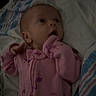baby, infant, pink_clothing, flamingo_pattern, blanket, bedding, striped_blanket, lying_down, hand_near_mouth, curious_expression, indoors, child, newborn, soft_lighting, portrait, sleepwear, cute, young_child, person, cozy