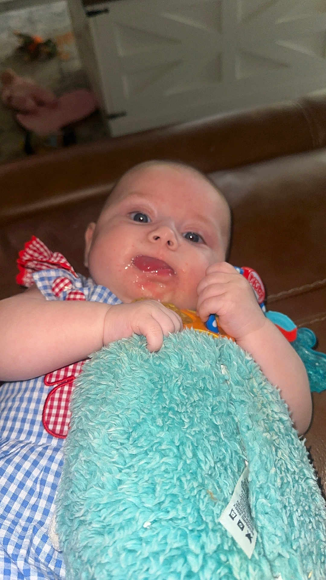 Oakley is registered to the contest to win money with this photo: baby, infant, blue_eyes, blanket, toy, hand, face, skin, clothing, pattern, red, blue, plush, comfort, indoor, person, cute, expression, child, toddler