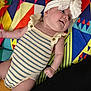 baby, bow, cheeks, child, colorful_blanket, cute, geometric_pattern, happy, headband, indoors, infant, knitted_outfit, lying_down, playful, portrait, relaxed, small_hands, smiling, soft_skin, striped_clothing