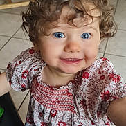 Mailey participe au concours pour gagner de l'argent avec cette photo : child, toddler, curly_hair, blue_eyes, smile, floral_dress, indoor, tile_floor, wooden_chair, person, cute, happy, portrait, young_child, clothing, baby, face, standing, casual, bright