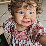 child, toddler, curly_hair, blue_eyes, smile, floral_dress, indoor, tile_floor, wooden_chair, person, cute, happy, portrait, young_child, clothing, baby, face, standing, casual, bright