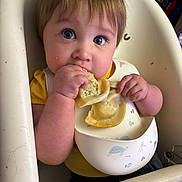 Atticus is registered to the contest to win money with this photo: baby, child, infant, high_chair, eating, food, messy_eating, bib, hands, face, blue_eyes, brown_hair, smiling, portrait, indoor, home, toys, balloons, feeding, lunchtime