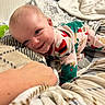 baby, child, smiling, pajamas, blanket, hand, blue_eyes, indoor, cute, cozy, infant, patterned_blanket, happy, person, portrait, lying_down, soft_texture, holiday_theme, warm, comfort