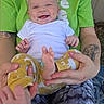 baby, smiling, adult, tattoo, elephant_tattoo, green_shirt, white_shirt, yellow_pants, barefoot, hands, legs, outdoor, happy, infant, person, holding, patterned_pants, closeup, playful, casual_clothing