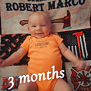 James joined the competition — help win amazing prizes! baby, infant, smiling, orange_onesie, quilt, axes, fire_department, text_overlay, name, lying_down, happy, cute, child, portrait, fabric, pattern, milestone, celebration, indoor, person