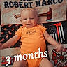 baby, infant, smiling, orange_onesie, quilt, axes, fire_department, text_overlay, name, lying_down, happy, cute, child, portrait, fabric, pattern, milestone, celebration, indoor, person