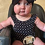 baby, child, high_chair, black_bow, headwrap, patterned_clothing, straps, chubby_cheeks, wide_eyes, curious, indoor, seat, furniture, person, infant, cute, expression, arm, legs, closeup