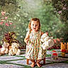 child, toddler, girl, portrait, outdoor, garden, flowers, teddy_bear, stuffed_animals, dress, butterfly_pattern, standing, smiling, barefoot, toys, toy_fence, play_area, colorful, storybook, photography
