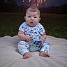 baby, child, infant, sitting, portrait, fireworks, night, outdoor, grass, blanket, water_bottle, drinking, clothing, patterned_shirt, pants, bare_feet, face, surprised_expression, celebration, photography