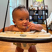 Isaiah joined the competition — help win amazing prizes! baby, jumper, snack, messy_face, indoor, wooden_floor, toy_shelf, face, smiling, child, home, cubicle_storage, tigers_picture, cheeky, graco, infant, curly_hair, playtime, candid, cheerful