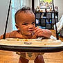 baby, jumper, snack, messy_face, indoor, wooden_floor, toy_shelf, face, smiling, child, home, cubicle_storage, tigers_picture, cheeky, graco, infant, curly_hair, playtime, candid, cheerful