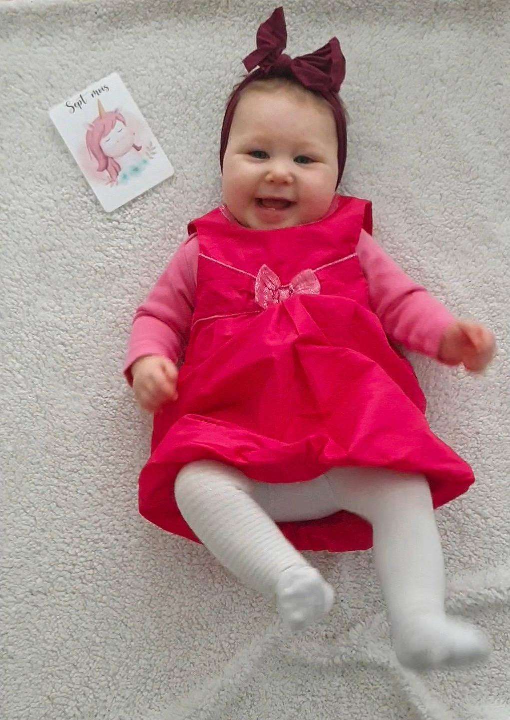 Riley a rejoint le concours — aidez-le/la à gagner de superbes lots ! baby, baby_toddler_clothing, cheek, child, costume, costume_hat, dress, face, fun, happy, hat, head, headgear, human_leg, magenta, person, pink, sitting, sleeve, smile