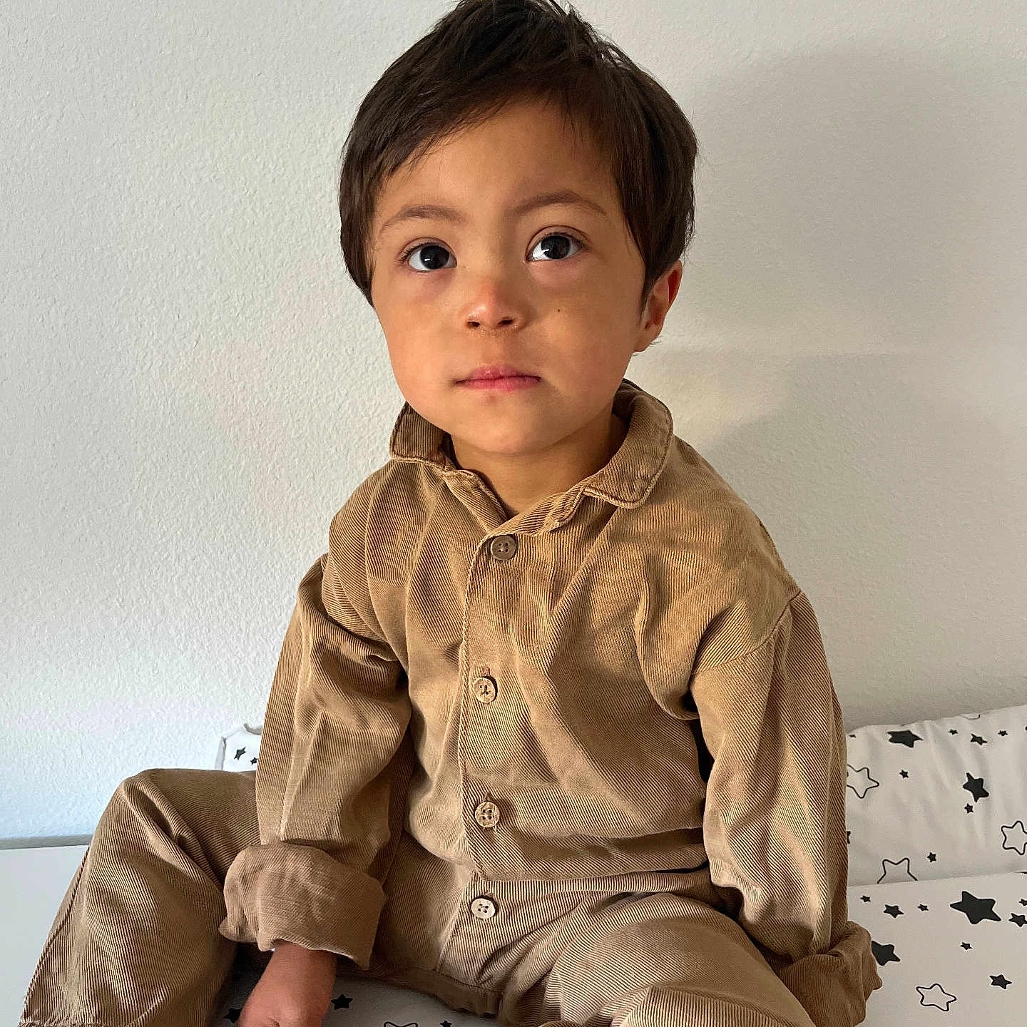 Simon-Léonard a rejoint le concours — aidez-le/la à gagner de superbes lots ! bed, bedspread, boy, brown_clothing, casual_wear, child, corduroy, cozy, cross_legged, curious_eyes, green_heart, indoors, neutral_expression, plain_wall, portrait, sitting, socks, star_pattern, white_socks, young_child