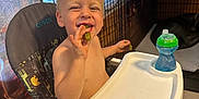 Colby joined the competition — help win amazing prizes! toddler, high_chair, pickle, smiling, indoor, child, blond_hair, sippy_cup, happy, eating, face, furniture, person, footwearless, window_blinds, dog_crate, plastic_tray, wood_paneling, tile_floor, home