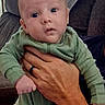 baby, child, infant, portrait, face, eyes, wide_eyed, serious_expression, green_outfit, onesie, clothing, held, adult_hand, arm, ring, couch, cushions, indoors, close_up, family