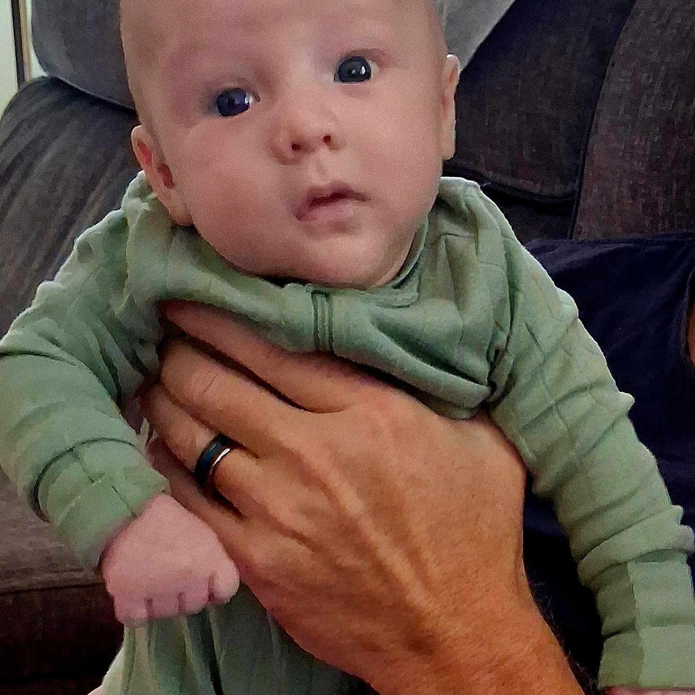Case joined the competition — help win amazing prizes! baby, child, infant, portrait, face, eyes, wide_eyed, serious_expression, green_outfit, onesie, clothing, held, adult_hand, arm, ring, couch, cushions, indoors, close_up, family